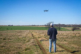 A student flies a drone over a grazing pasture to record the amount of light reflected in key wavelengths associated with plant health characteristics. 